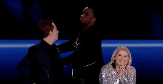 Man pointing toward a woman on a dark television set