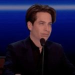 Man speaking into a microphone against a blue backdrop