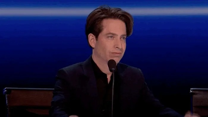 Man speaking into a microphone against a blue backdrop