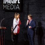 Two speakers on stage in front of an iHeartMedia sign