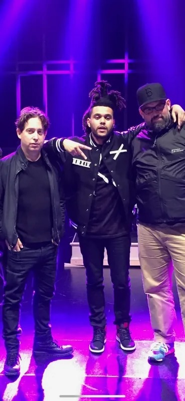 Three performers standing on a purple-lit stage
