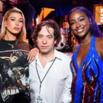 Man in a lanyard posing between two women at a concert