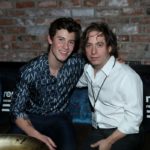 Two men seated together in front of a record label backdrop