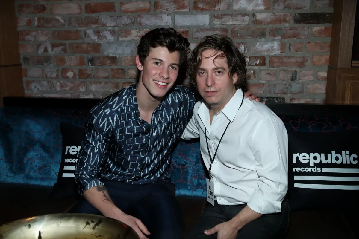 Two men seated together in front of a record label backdrop