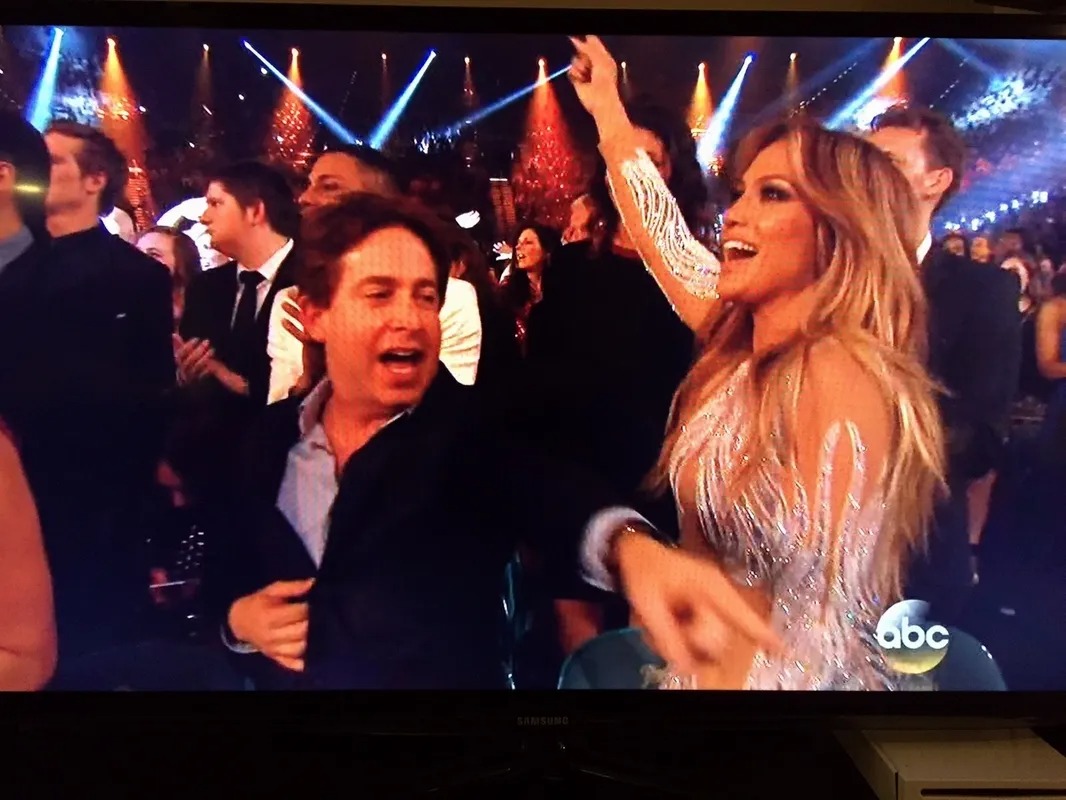 Man in an awards show audience with a performer nearby