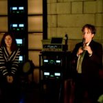 Man speaking into a microphone in a dim lounge