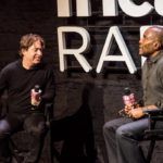 Two men talking on stage in front of an iHeart Radio sign