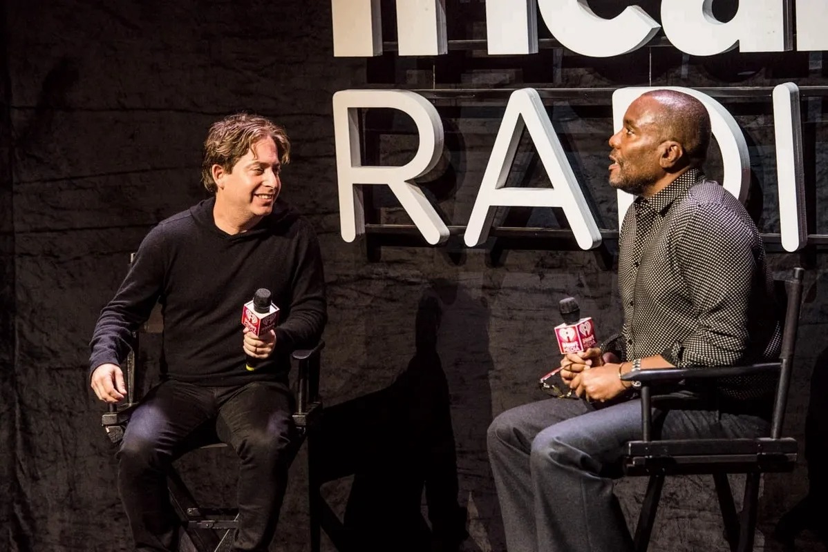 Two men talking on stage in front of an iHeart Radio sign