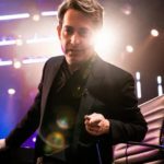 Man in a black suit walking across a stage under lights