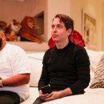 Two men sitting on a white sofa in a living room