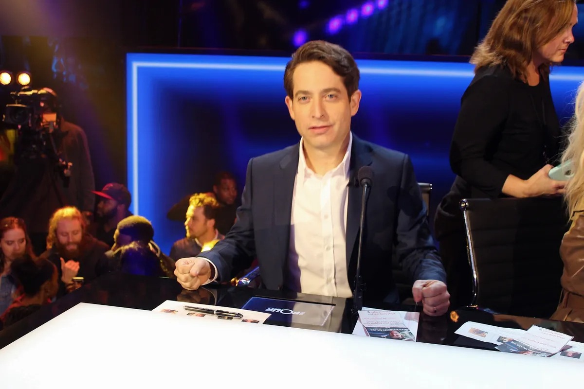 Man in a navy suit at the desk with crew nearby
