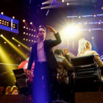Man on a lit stage gesturing toward a judge