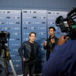 Camera crew filming a man in front of a press backdrop