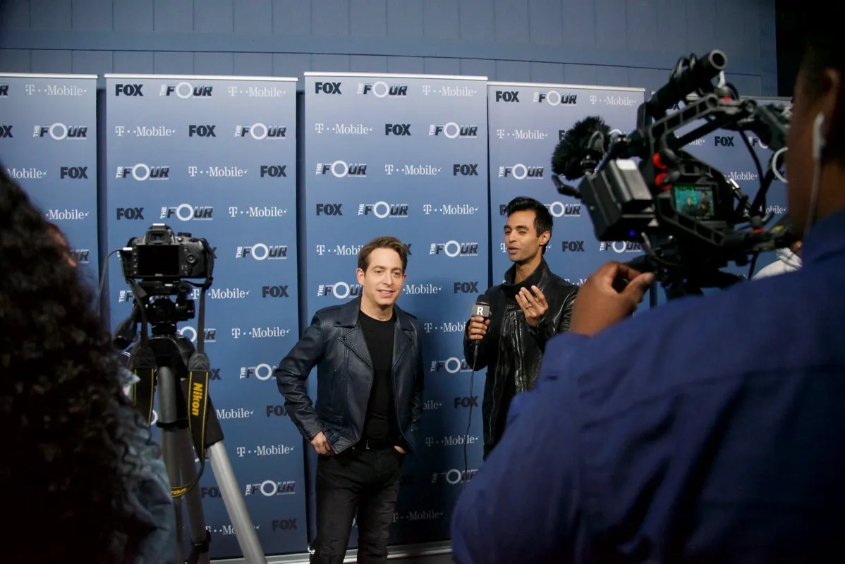 Camera crew filming a man in front of a press backdrop