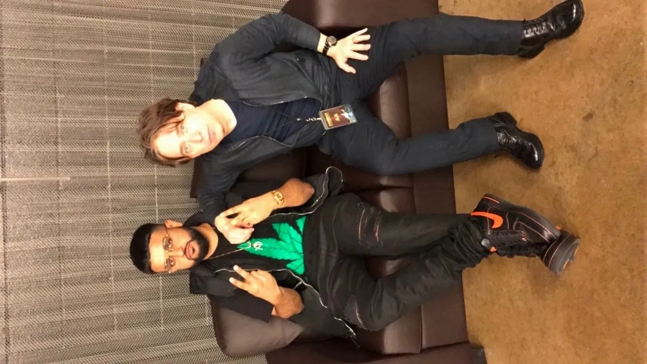 Two men sitting on a bench against a wall