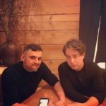 Two men sitting at a wooden table with a phone