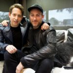Two men in leather jackets sitting together on a couch