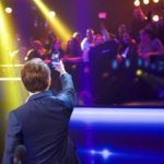 Man raising a phone toward stage lights and the audience