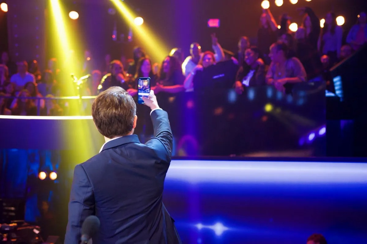 Man raising a phone toward stage lights and the audience
