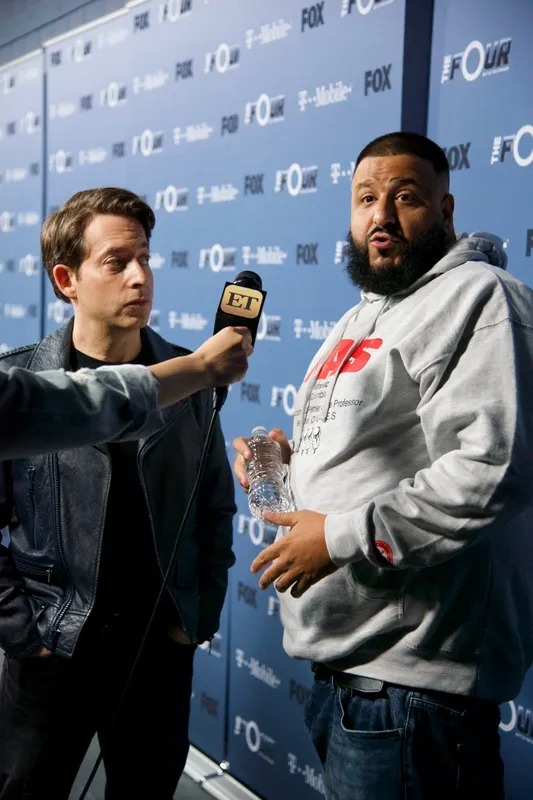 Man interviewing a guest in front of a press wall