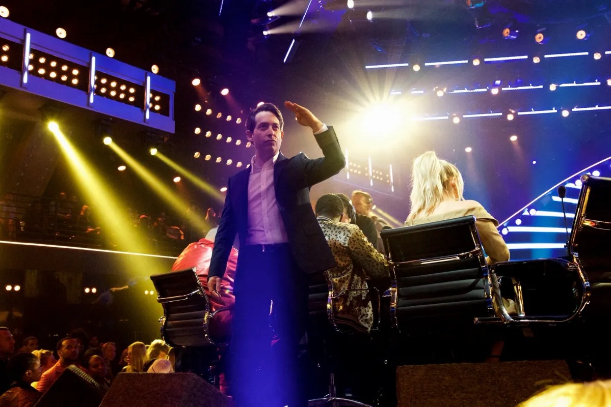 Performer standing center stage beside a seated judge