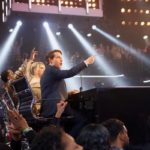 Man on stage pointing to the crowd under spotlights