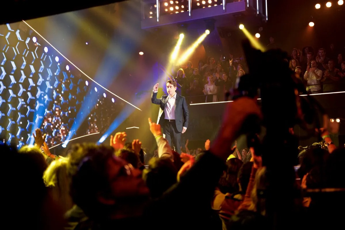 Performer singing on stage with crowd silhouettes in front