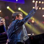 Man raising his hand toward the audience under stage lights