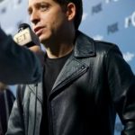 Man in a leather jacket speaking into a microphone at a press event