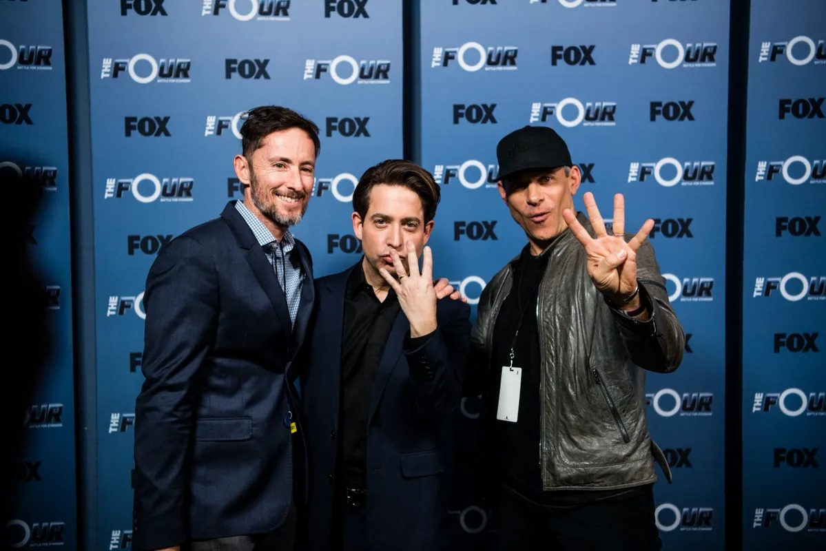 Three men posing together on a press wall