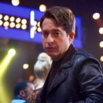 Man in a leather jacket in front of stage lights