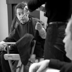 Black and white photo of a man in a makeup chair backstage