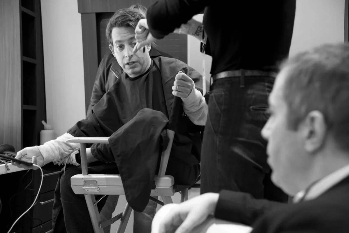 Black and white photo of a man in a makeup chair backstage