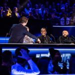 Panel of judges seated at a glowing desk before an audience