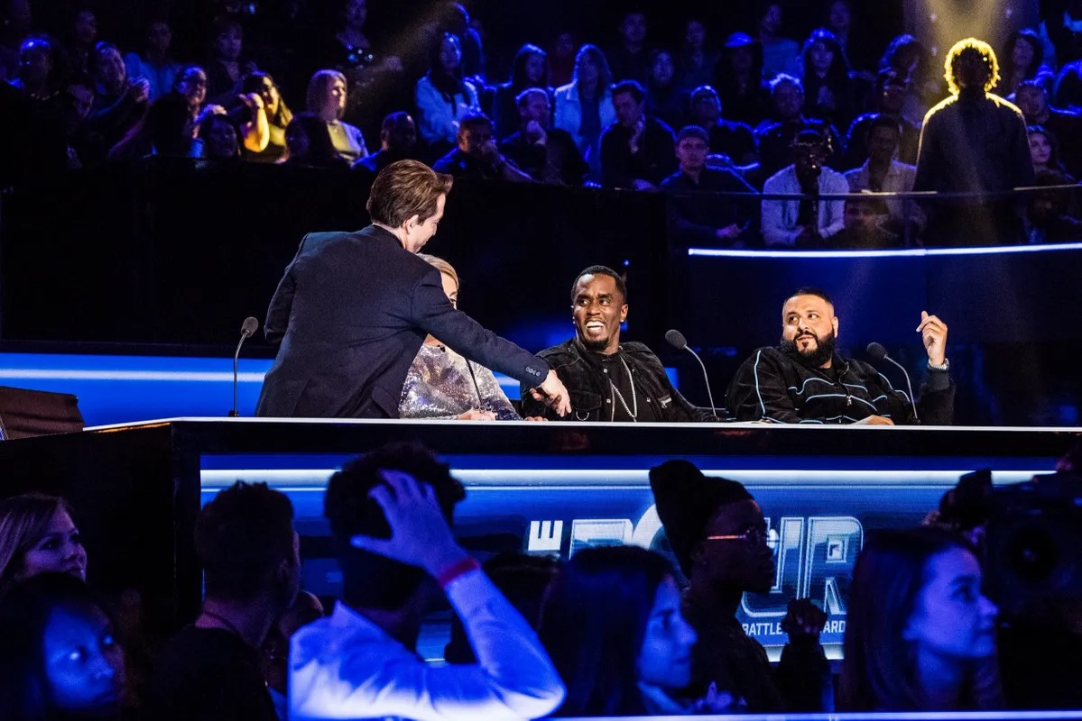 Panel of judges seated at a glowing desk before an audience